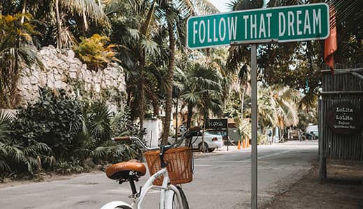 Follow that Dream sign on a post with a white bicycle that has a basket beside it (certified professional career coach)