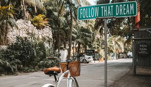 Follow that Dream sign on a post with a white bicycle that has a basket beside it (certified professional career coach)